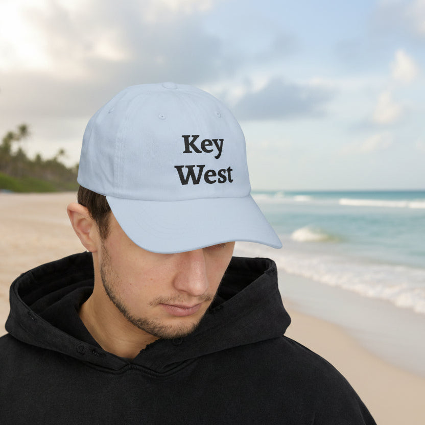 Person wearing a 'Key West' cap on a beach with palm trees and ocean in the background