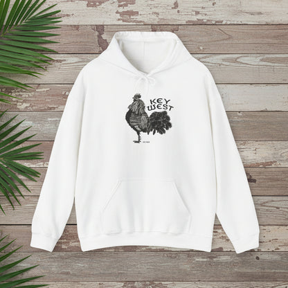 White hoodie with rooster graphic and 'Key West' text on a wooden surface with palm leaves.