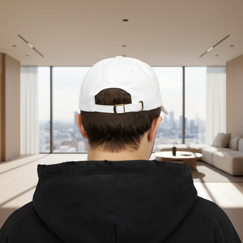 Person wearing a white cap with a logo, standing in a modern living room with large windows.