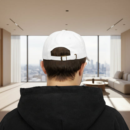 Person wearing a white cap with a logo, standing in a modern living room with large windows.