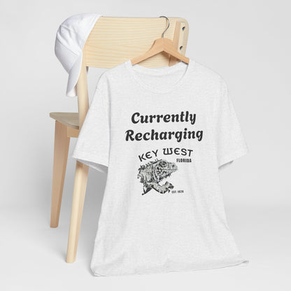 White t-shirt with 'Currently Recharging Key West Florida' text and graphic on a wooden chair.