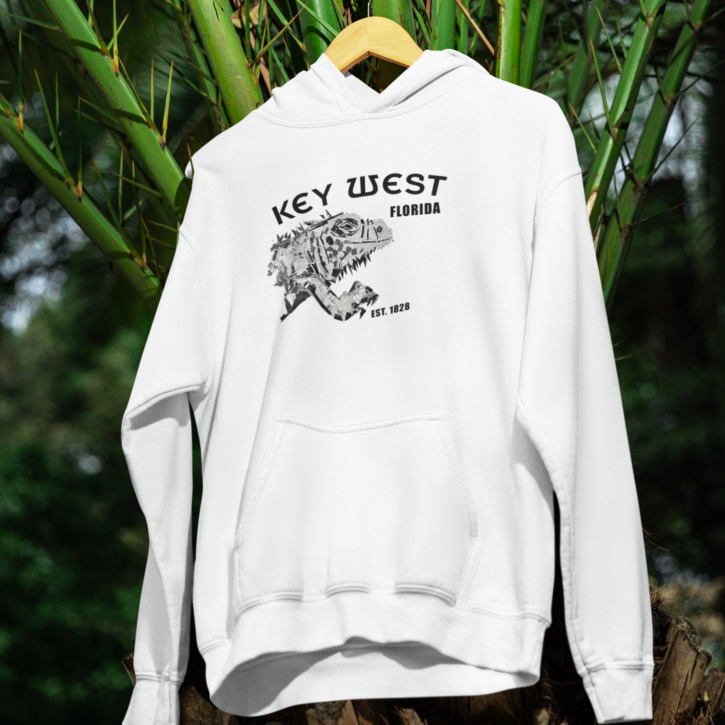 White hoodie with 'Key West, Florida' text and iguana graphic on a hanger against a natural background.