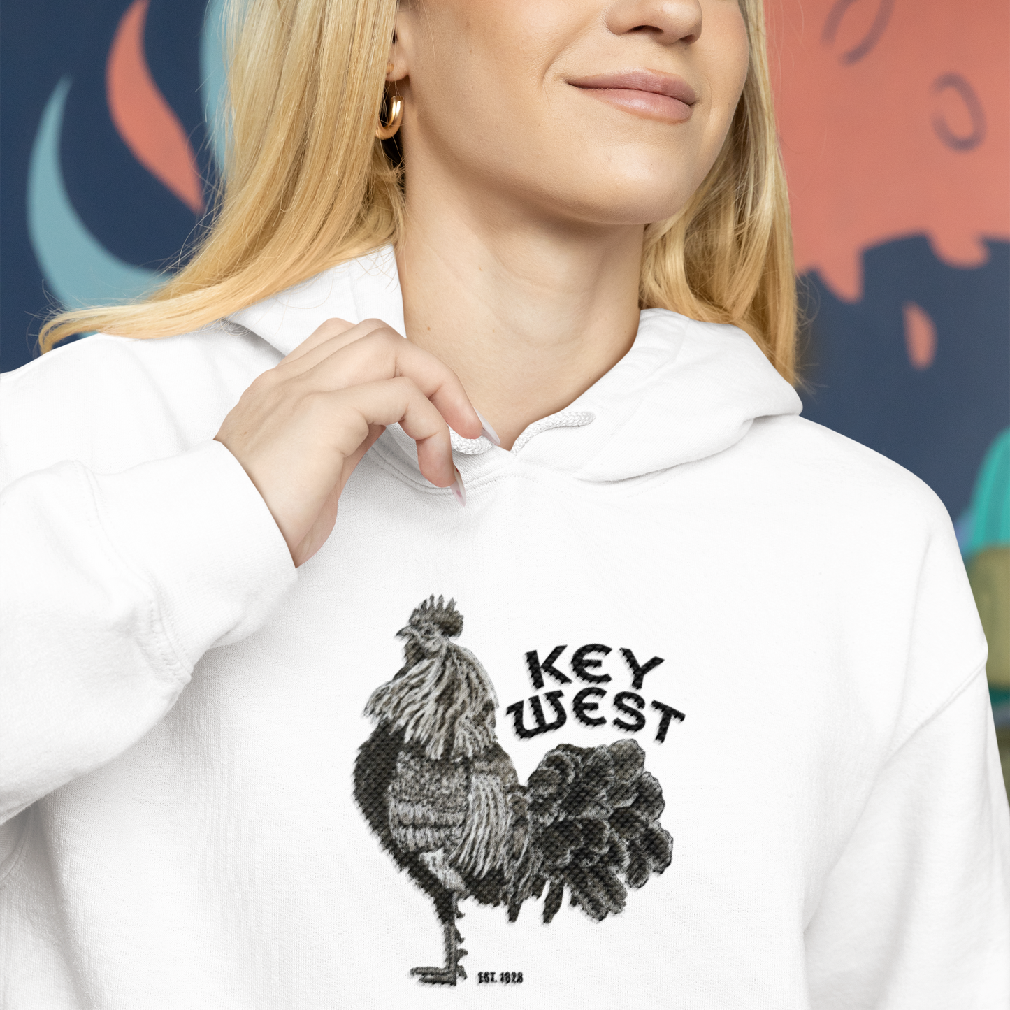 Person wearing a white hoodie with a rooster graphic and 'Key West' text against a colorful abstract background.